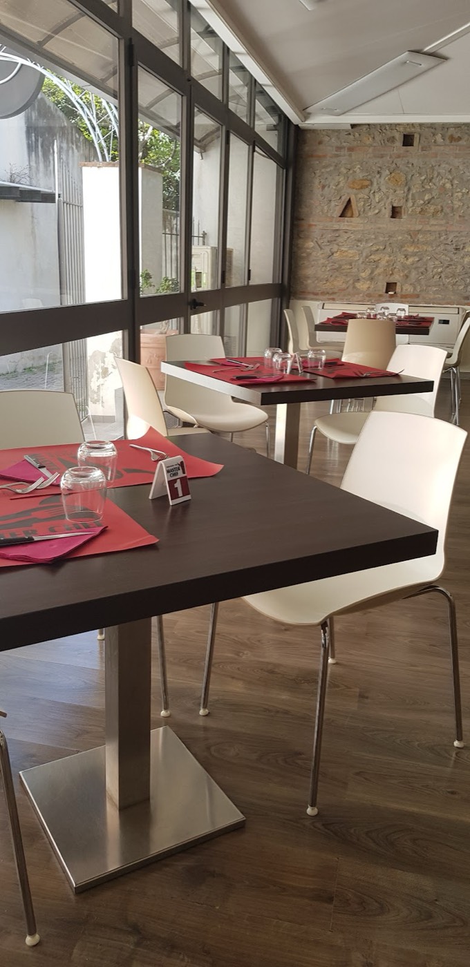 Sala interna con tavoli in legno, sedie bianche e parete in pietra a vista